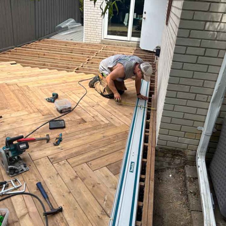 A construction worker measures and installs finishing touches on a deck, focusing on precision and detail to ensure a high-quality finish.