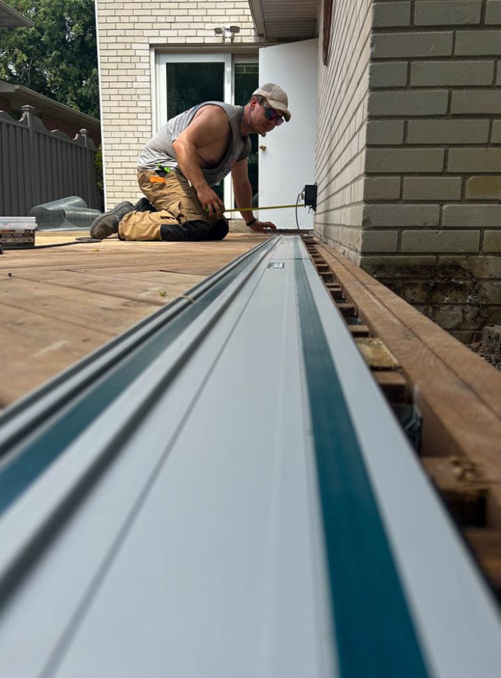 Detailed view of a deck construction process with a worker focused on measuring and cutting wooden boards, showcasing the intricacy and precision required.