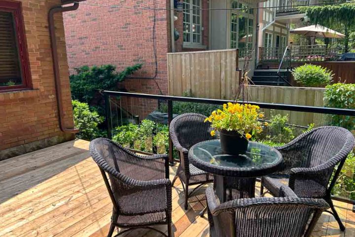 A charming outdoor seating arrangement on a wooden deck with a centerpiece table and flowering plant, offering a tranquil spot for relaxation and entertainment.