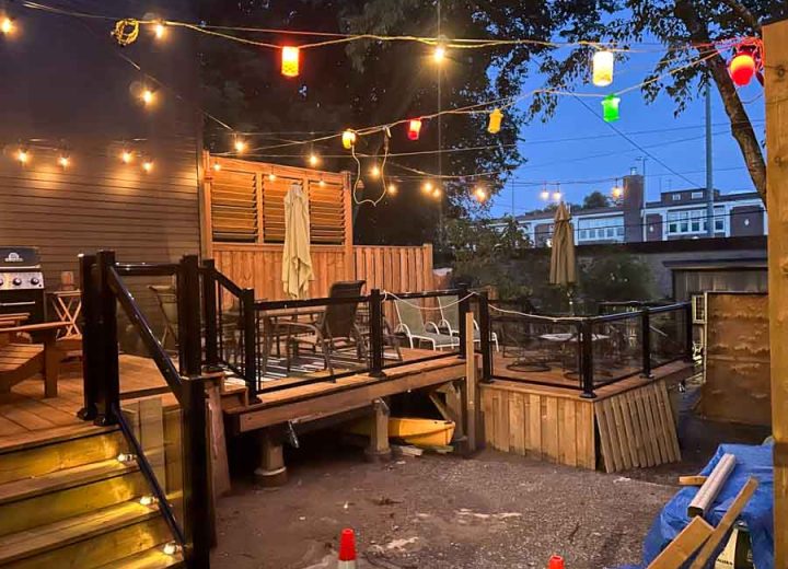 A beautifully illuminated deck at night featuring colorful string lights, with a wood-and-metal railing, creating a warm and inviting outdoor space.